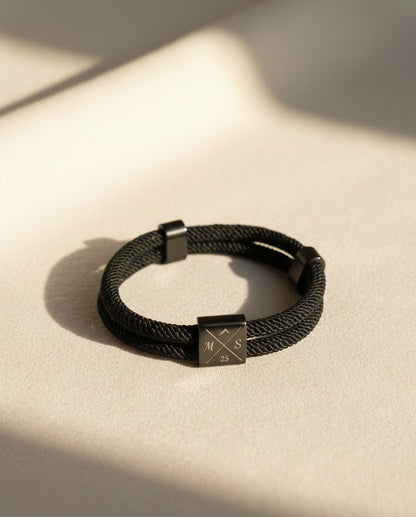 Black braided bracelet with a square clasp on a beige surface
